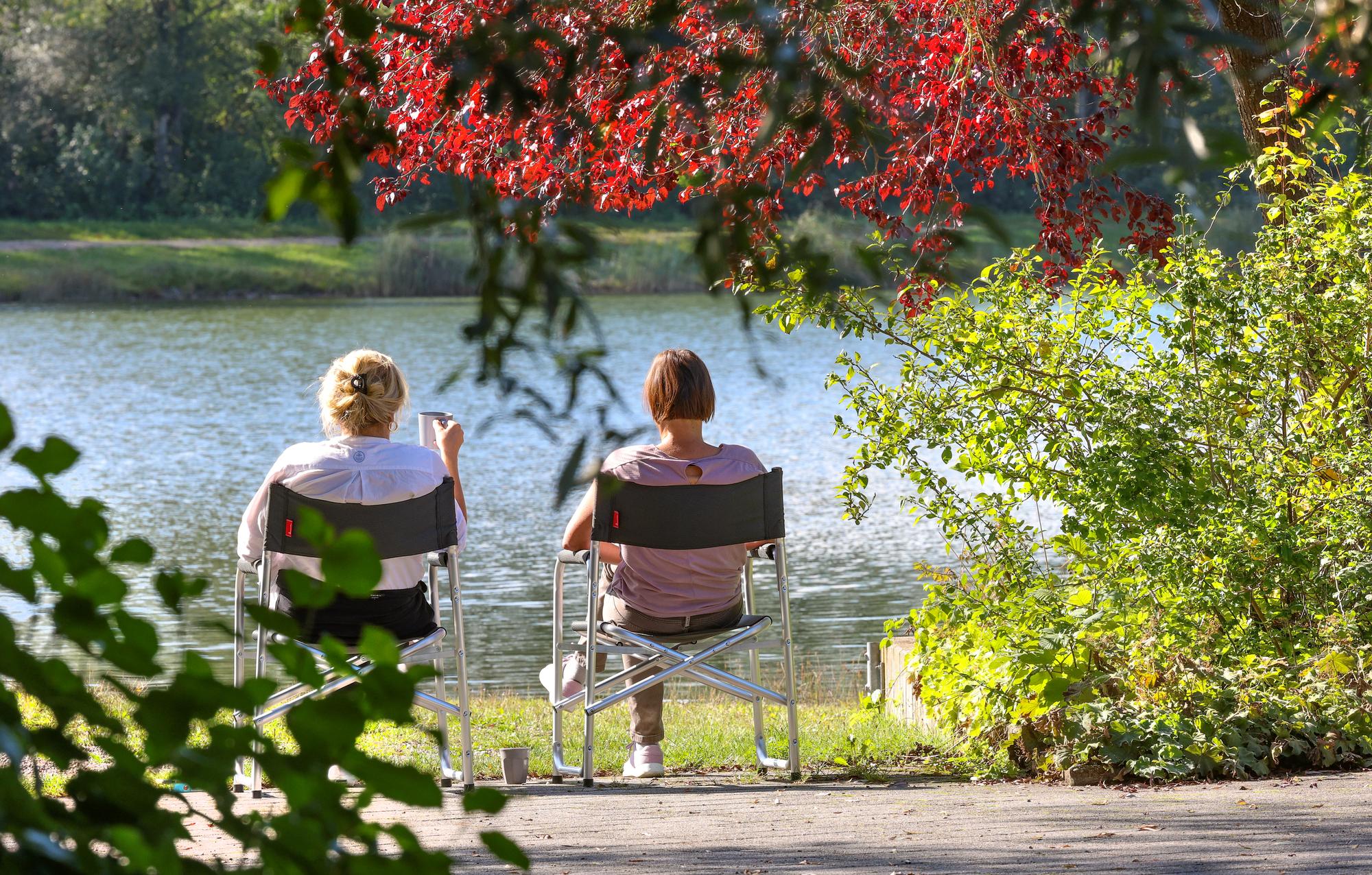 24.09.2023, Baden-Württemberg, Ertingen: Zwei Frauen sitzen auf Campingstühlen an einem See in der Sonne. Foto: Thomas Warnack/dpa +++ dpa-Bildfunk +++ (KEYSTONE/DPA/Thomas Warnack)