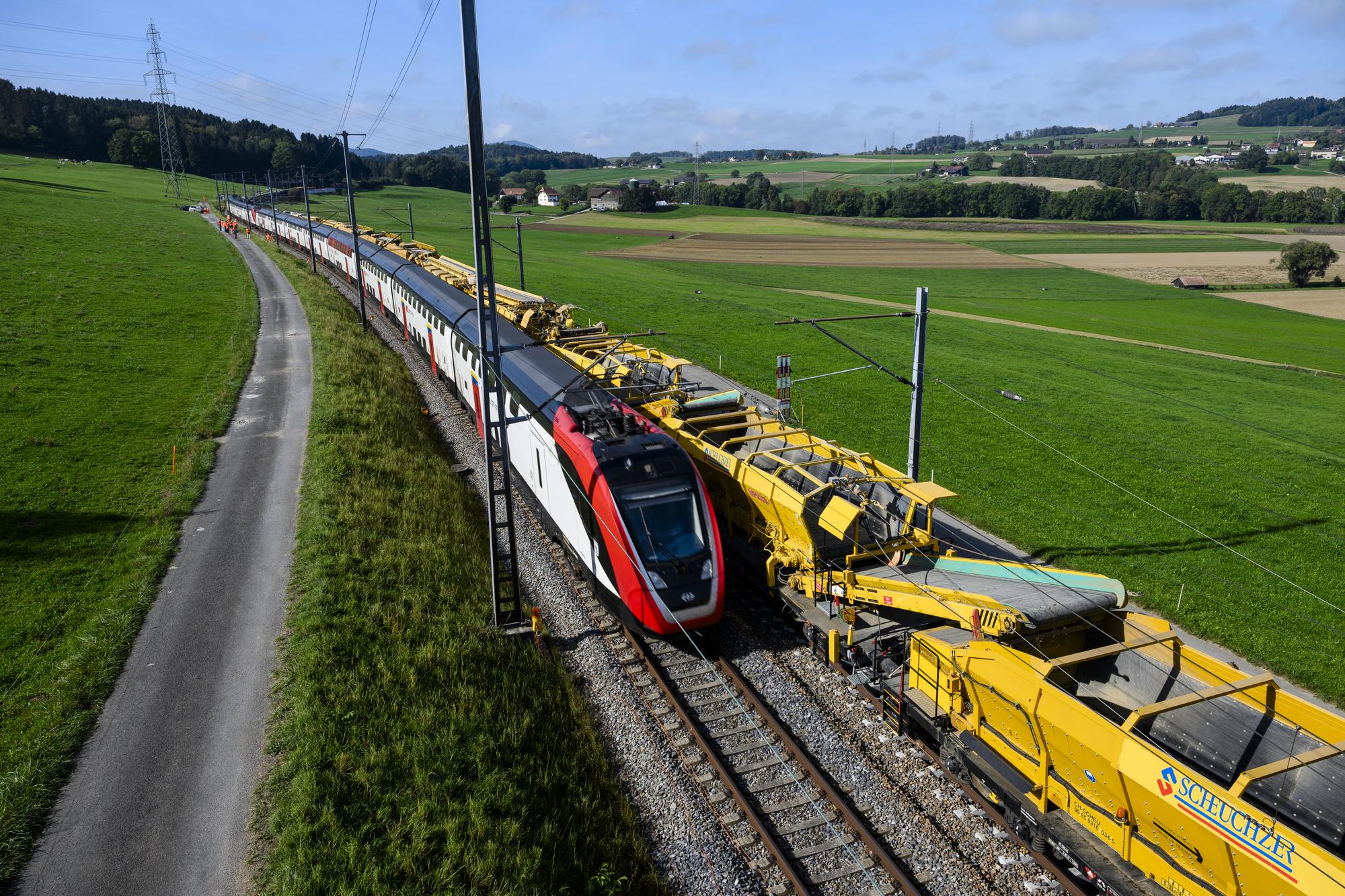 Un train Duplex TGL des CFF circule a cote de la machine "Puscal" de l'entreprise Scheuchzer lors d'une visite de presse sur le chantier d'entretien des voies CFF de 7km de long entre Puidoux et Palezieux le jeudi 5 octobre 2023 pres de la gare de Palezieux. (KEYSTONE/Jean-Christophe Bott)