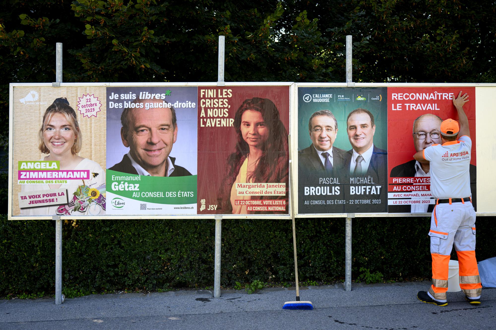 Carlos Andrade, afficheur de la societe APG | SGA colle les affiches electorales pour les elections pour les representant vaudois au Conseil des Etat, de gauche a droite, Angela Zimmermann (Jeunes Verts), Emmanuel Getaz (Les Libres), Margarida Janeiro (JSY), Pascal Broulis (PLR), Michael Buffat (UDC) et Pierre-Yves Maillard (PS), lors la campagne pour les elections federales ce lundi 25 septembre 2023 a Lausanne. (KEYSTONE/Laurent Gillieron)