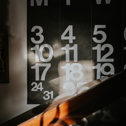 A large wall calendar is illuminated by warm sunbeams.