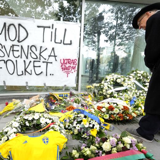 Floral tributes, a Swedish team jersey, and notes of condolence are placed on the pavement and a sign reads 'courage to the Swedish people' during a commemoration for the victims of a shooting in the center of Brussels, Wednesday, Oct. 18, 2023. Police in Belgium on Tuesday shot dead a suspected Tunisian extremist accused of killing two Swedish soccer fans in a brazen attack on a Brussels street. (AP Photo/Martin Meissner)