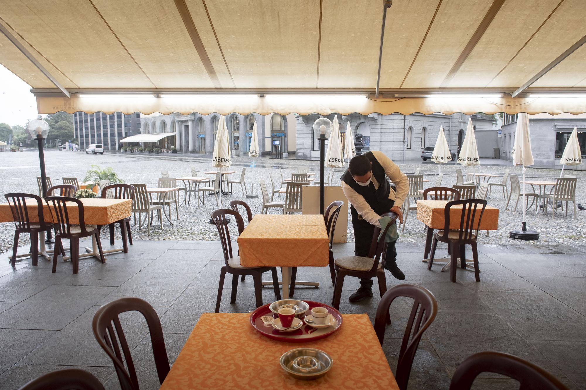 A waiter desinfects chairs at the restaurant Portico on the Piazza Grande in Locarno, Switzerland, Monday, May 11, 2020. Switzerland reopens it's shops, fitness centers, restaurants and museums under strict restrictions for social distancing and hygiene measures today. (KEYSTONE/Ti-Press/Pablo Gianinazzi)