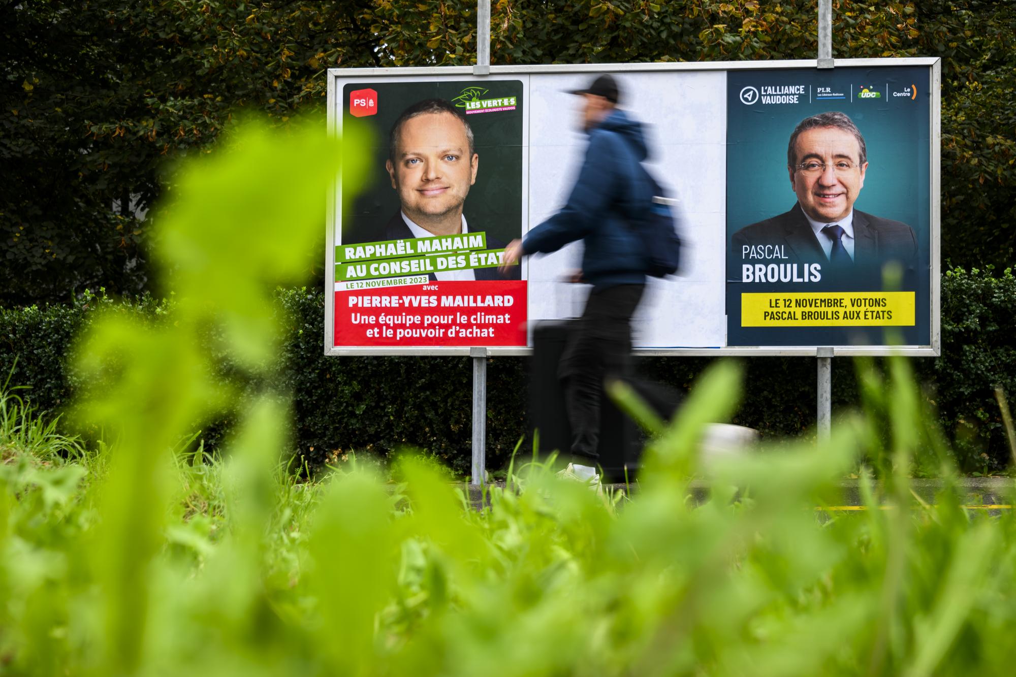 Une personne marche devant les affiches pour le 2eme tour du Conseil des Etats des elections federales, dans le canton de Vaud, avec le candidat Raphael Mahaim (Parti socialiste vaudois - Les Vert.e.s vaudois.es) et Pascal Broulis (L'Alliance vaudoise, PLR - UDC - Le Centre) le vendredi 27 octobre 2023 a Lausanne. (KEYSTONE/Jean-Christophe Bott)