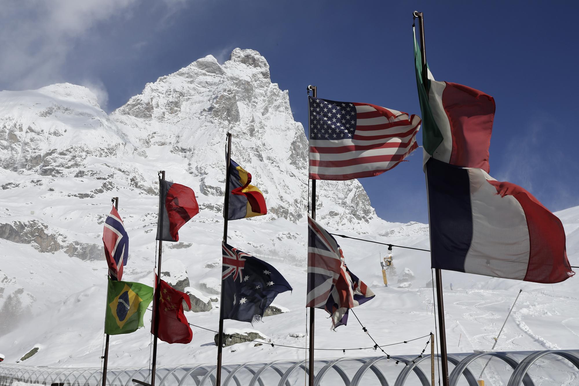 The Matterhorn mountain is seen behind flags of different countries as strong wind blows by the course of an alpine ski, men's World Cup downhill race after it was canceled, in Cervinia-Zermatt, Saturday, Nov. 11, 2023. The inaugural World Cup downhill at the storied Matterhorn mountain will have to wait at least one more day after a race Saturday was canceled because of heavy snowfall and strong winds. Race organizers called off plans for the men's downhill soon after 6 a.m. local time at the new Gran Becca course that starts in Switzerland and finishes in Italy. (AP Photo/Marco Trovati)