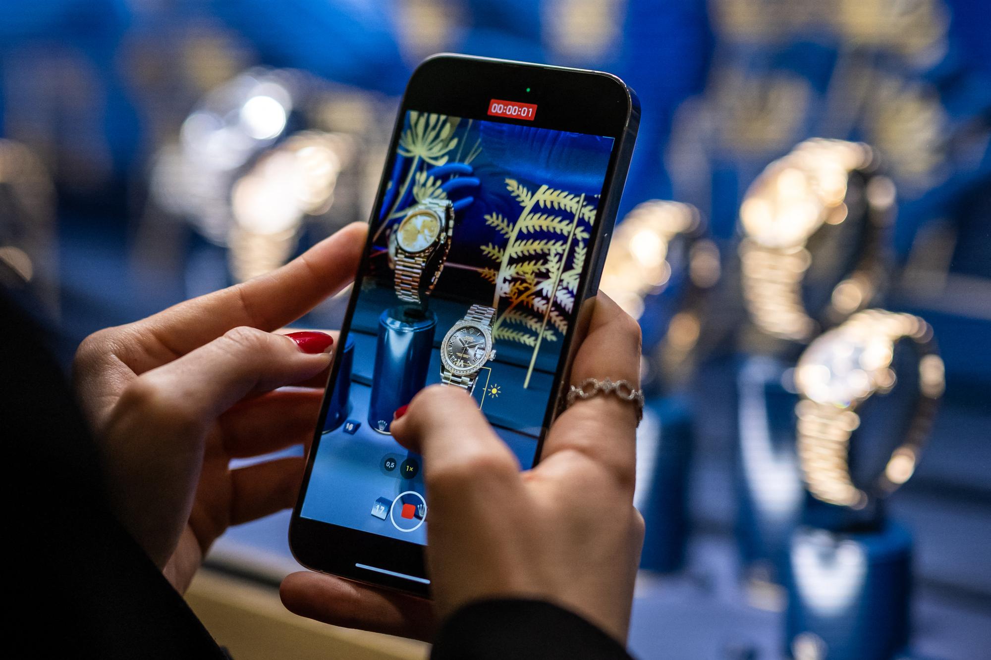 A woman films watches with her mobile phone at the Rolex booth during the luxury watch fair 'Watches and Wonders Geneva', in Geneva on March 27, 2023. (Photo by Fabrice COFFRINI / AFP)