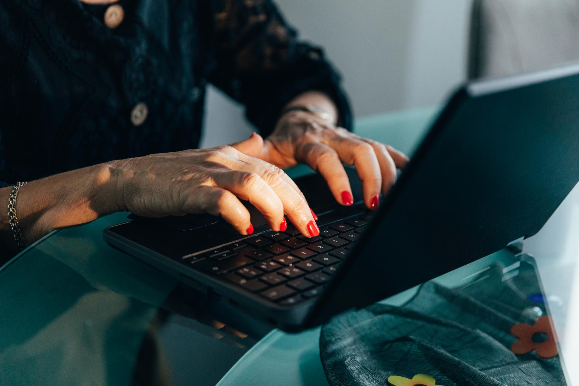 Close up of senior female hands with red nail polish typing on the laptop.