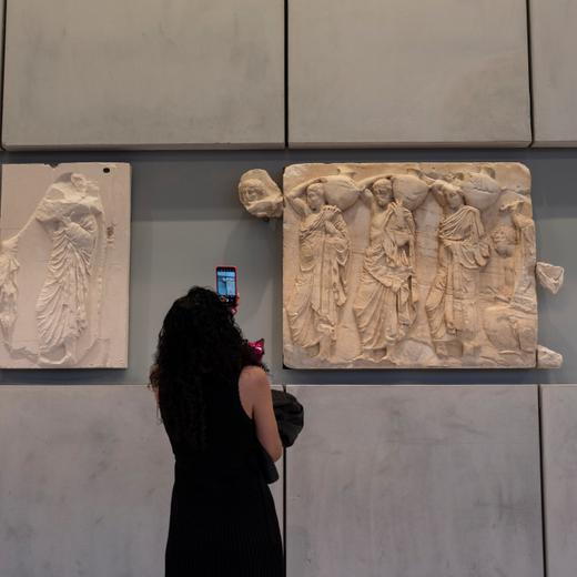 A woman takes a pictures of a newly placed male head on the frieze of the Acropolis museum during a ceremony for the repatriation of three sculpture fragments, in Athens, on Friday, March 24, 2023. Greece received three fragments from the ancient Parthenon temple that had been kept at Vatican museums for two centuries. Culture Ministry officials said the act provided a boost for its campaign for the return of the Parthenon Marbles from the British Museum in London. (AP Photo/Petros Giannakouris)