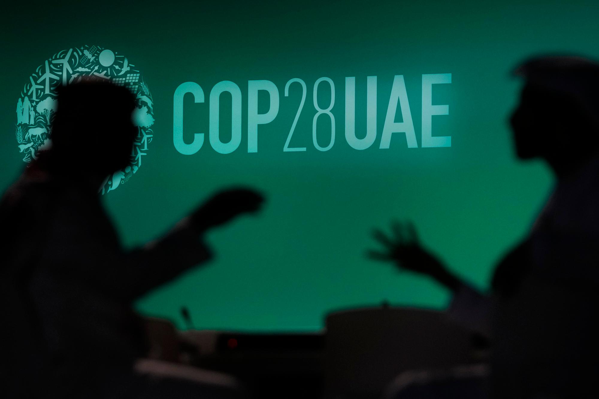 People are silhouetted against a logo for the COP28 U.N. Climate Summit, Wednesday, Nov. 29, 2023, in Dubai, United Arab Emirates. (AP Photo/Rafiq Maqbool)