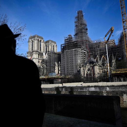 Pedestrians look at workers operating on scaffoldings around the wooden structure of the new spire in place at Notre-Dame de Paris Cathedral, on the Ile de la Cite in Paris, on December 2, 2023 during reconstruction work. This spire is being reconstructed to be identical to the original one, destroyed in the fire of April 15, 2019 with the Cathedral set to be reopened at the end of 2024 according to the French Minsitry of Culture. (Photo by JULIEN DE ROSA / AFP)