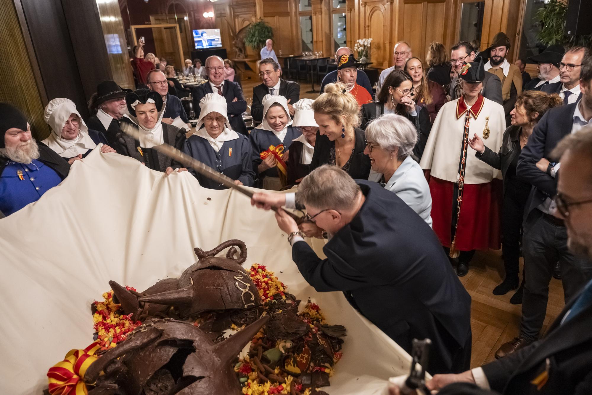 Nationalrat Daniel Sormanni, MCG-GE, Bundesraetin Elisabeth Baume-Schneider und die Genfer Regierungsraetin Delphine Bachmann, von unten, zerschlagen bei der Zeremonie der Escalade den Schokolagekessel, die Marmite, am Rand der Wintersession der Eidgenoessischen Raete, am Montag, 11. Dezember 2023 in der Galerie des Alpes im Bundeshaus in Bern. Die Escalade erinnert in Genf an die erfolgreiche Verteidigung der Genfer Bevoelkerung gegen die Savoyer, die im Jahr 1602 unter Charles-Emmanuel Ier Genf einnehmen wollten. (KEYSTONE/Alessandro della Valle)