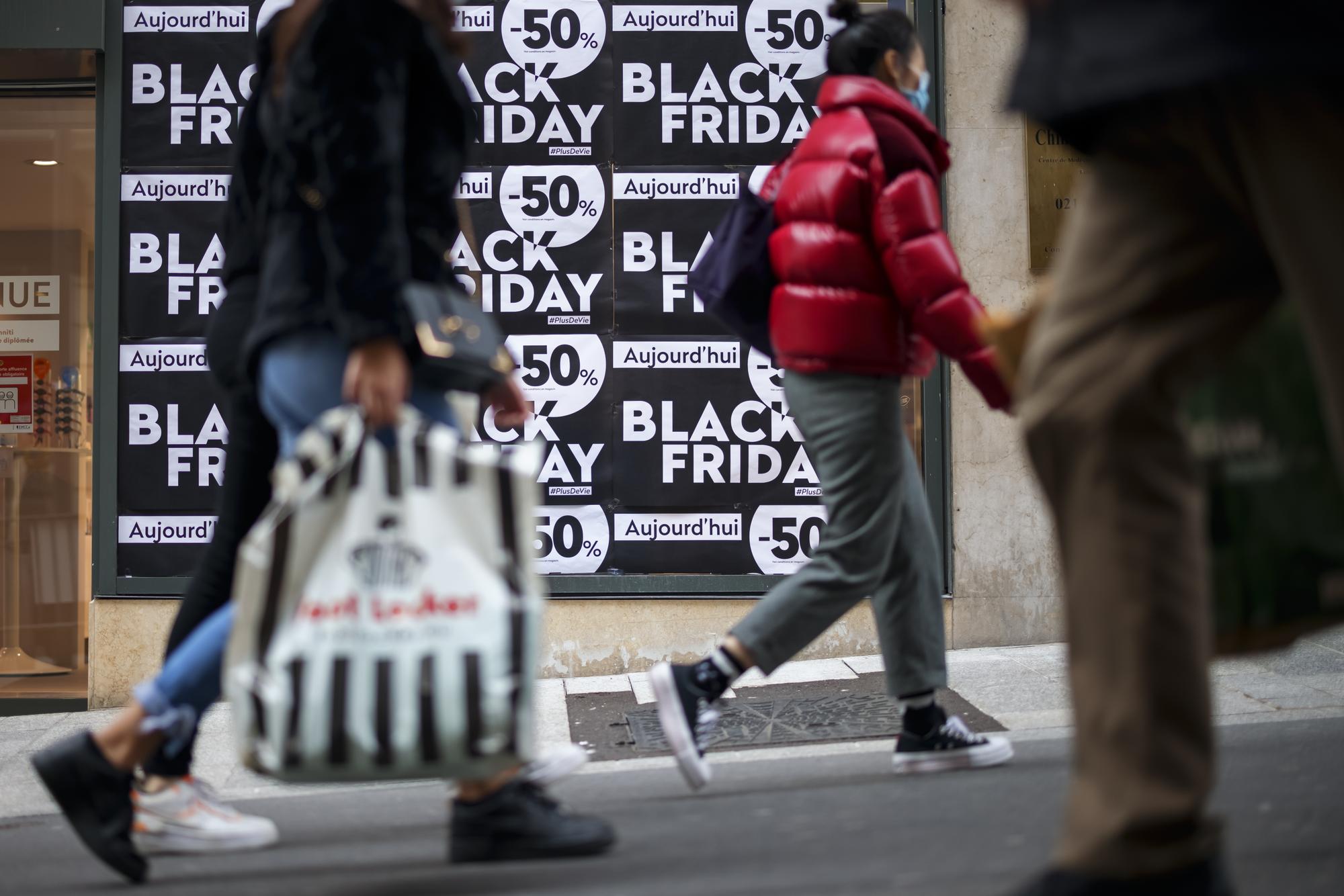 Des passants marchent avec leurs achats devant un magasin a l'occasion de la journee de soldes du "Black Friday" le vendredi 27 novembre 2020 a Lausanne. (KEYSTONE/Valentin Flauraud)