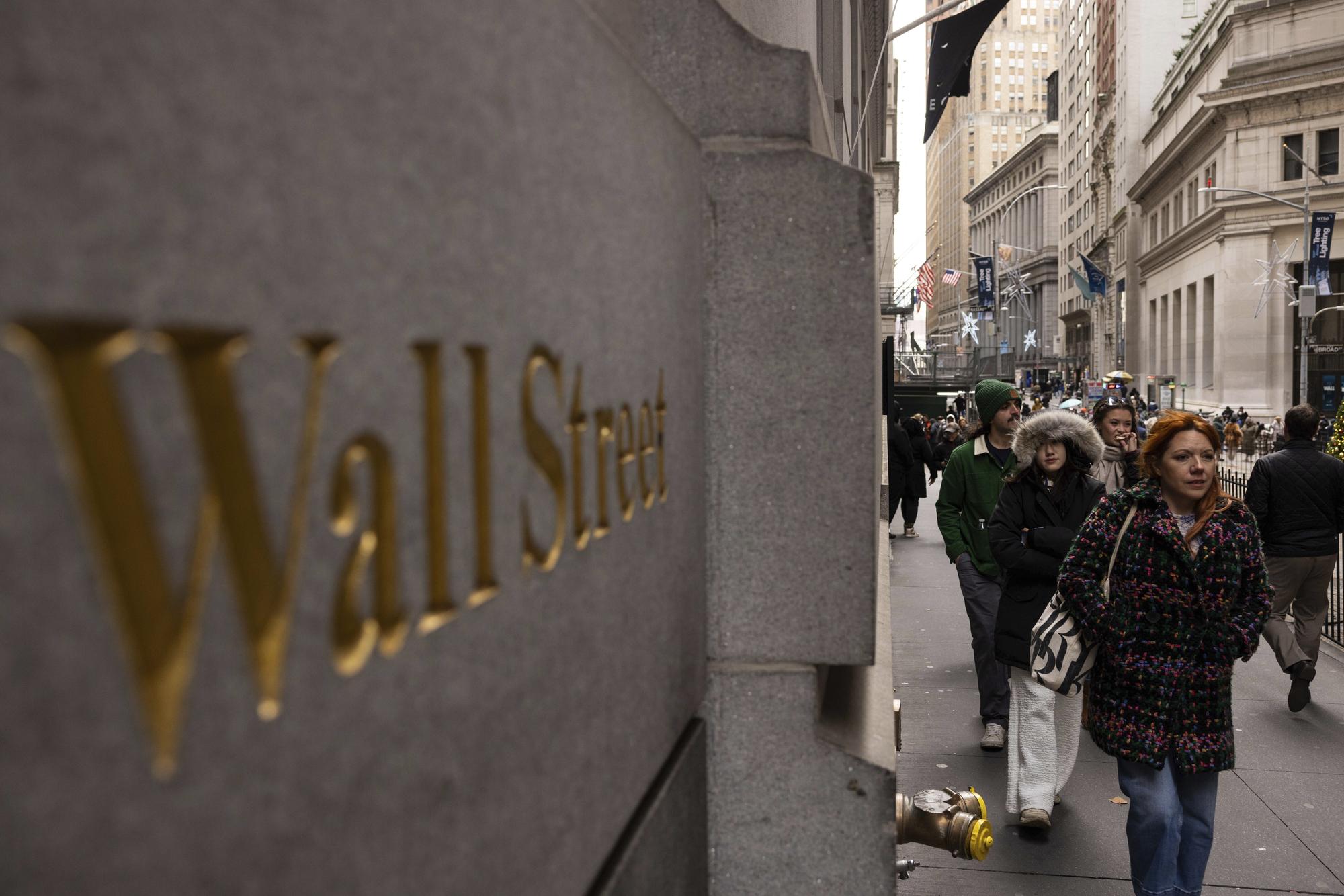 People walk past a Wall Street sign outside the New York Stock Exchange, Monday, Dec. 11, 2023, in New York. Wall Street is inching up modestly Wednesday ahead of a decision by the U.S. Federal Reserve on interest rates.(AP Photo/Yuki Iwamura)