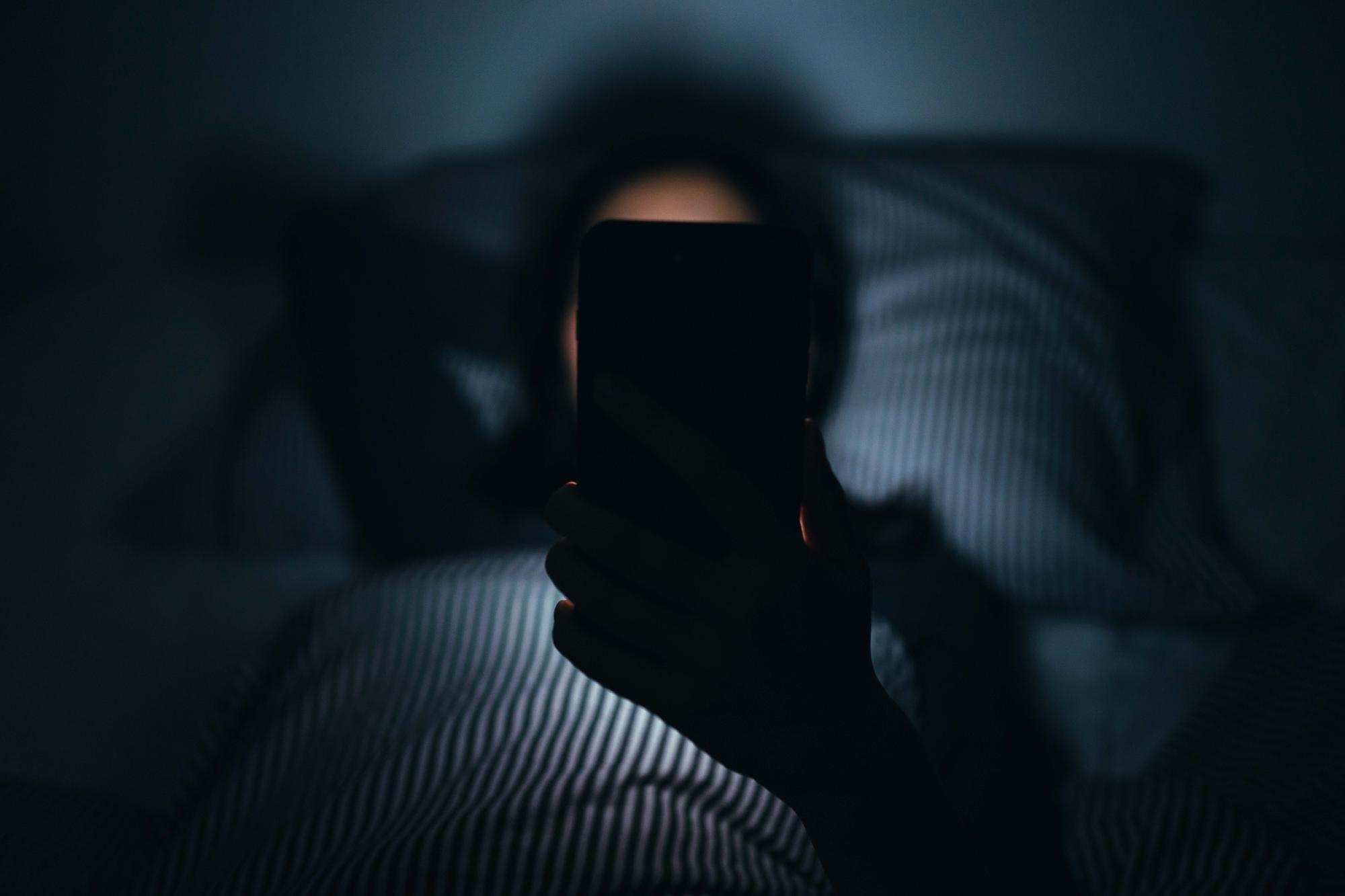 Woman texting and reading on smartphone while lying in bed in midnight