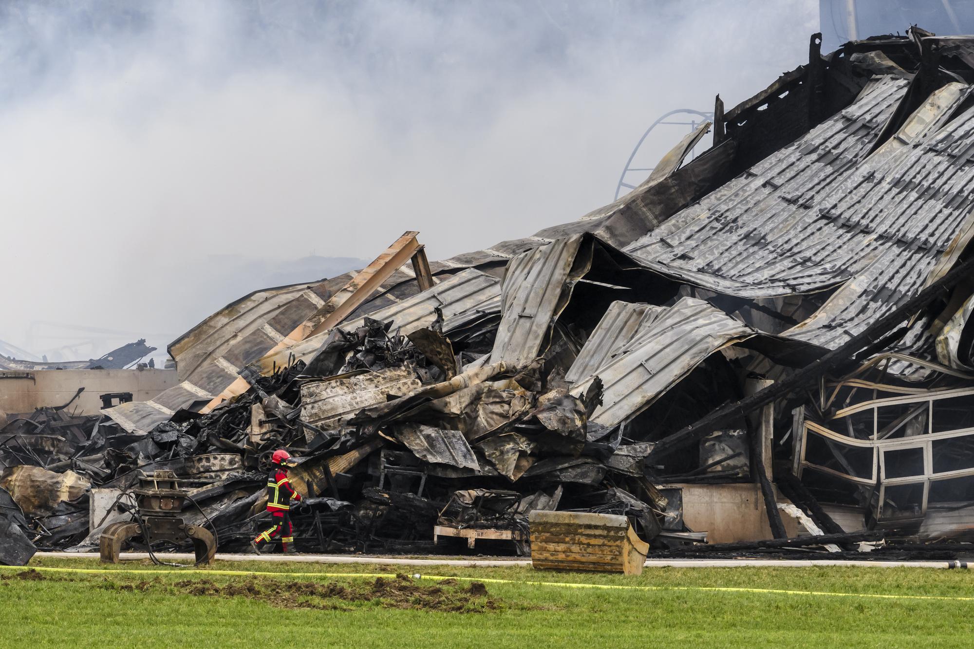 Un pompier marche autour des decombres apres l'incendie d'une ferme le jeudi 21 decembre 2023 a Bottens dans le canton de Vaud. Plus de 500 animaux, principalement des bovins adultes et des veaux, ont peri dans l'incendie qui a ravage une ferme a Bottens dans la nuit de mercredi a jeudi. Une personne qui residait dans le rural est toujours recherchee. (KEYSTONE/Jean-Christophe Bott)