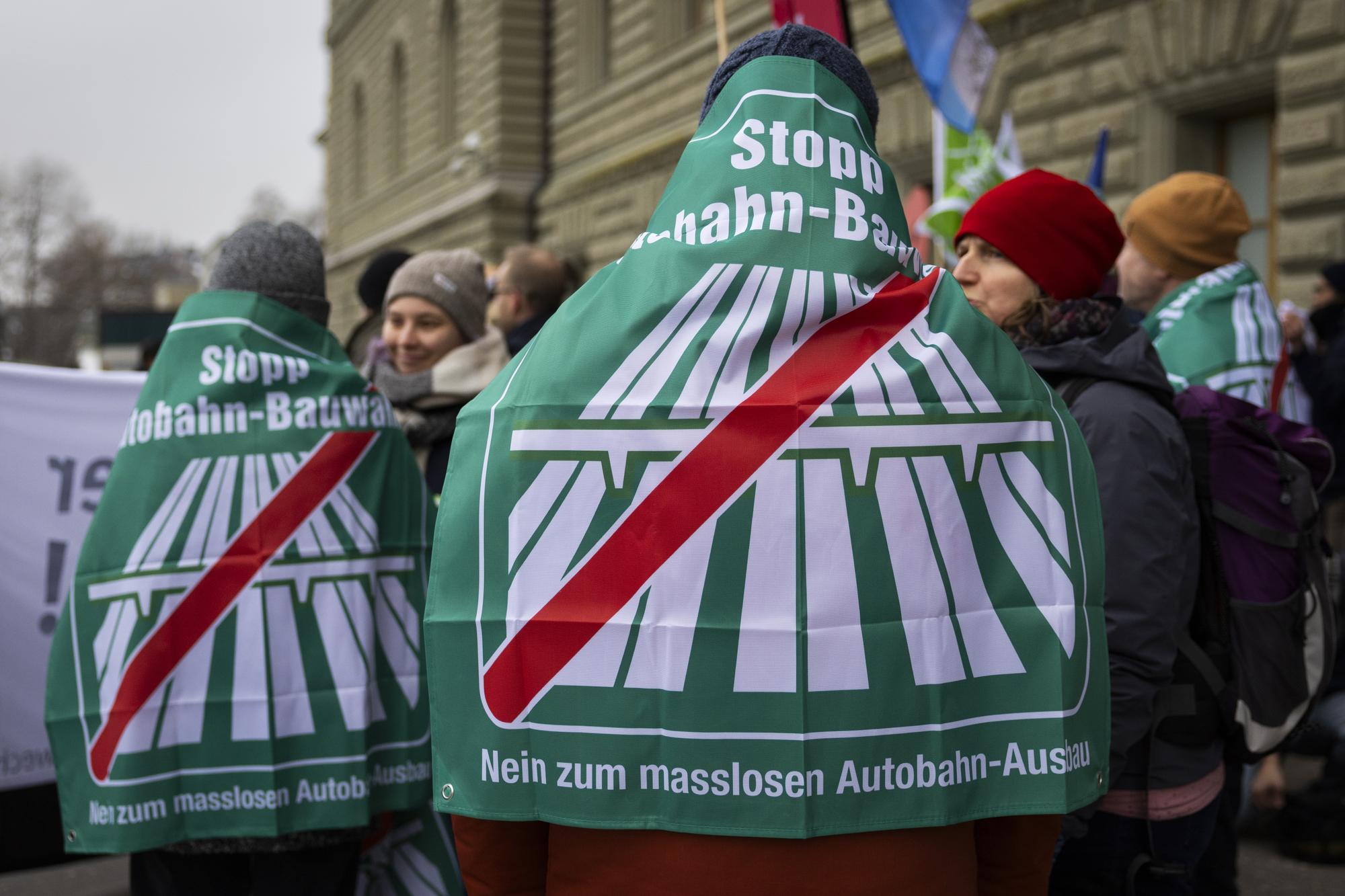 Unterstuetzer tragen Fahnen bei der Einreichung der Unterschriften fuer das Referendum "Stopp Autobahn-Bauwahn, Nein zum masslosen Autobahn-Ausbau", am Donnerstag, 11. Januar 2024 vor der Bundeskanzlei in Bern. (KEYSTONE/Peter Klaunzer)