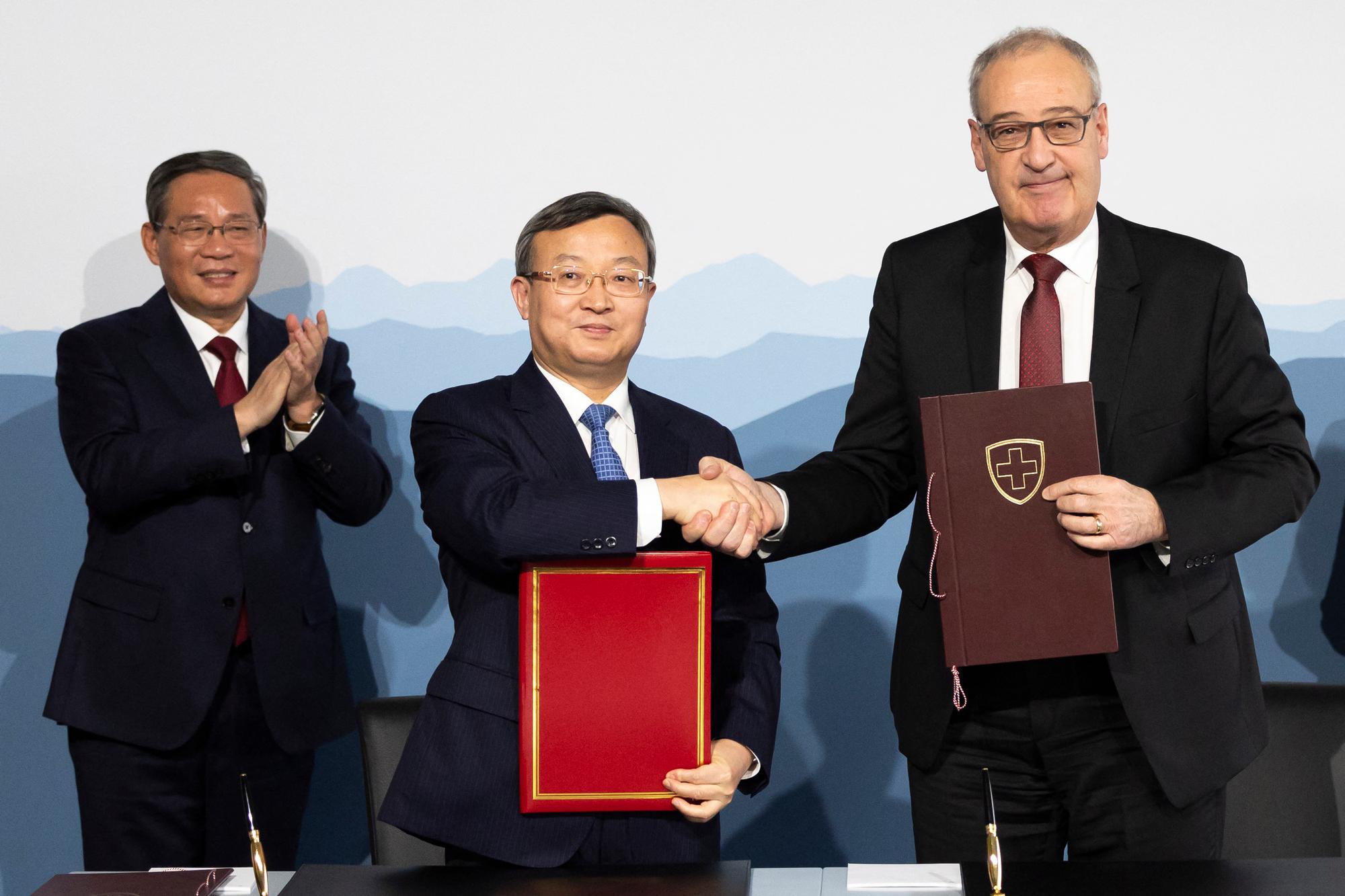 Swiss Federal Minister Guy Parmelin (R) and Chinese Vice Minister of the Ministry of Commerce Wang Shouwen (C) shake hands after signing a joint statement of the free trade agreement beside Prime Minister of the People's Republic of China Li Qiang (L), during an official visit in Kehrsatz near Bern on January 15, 2024. China's Prime Minister is visiting Switzerland to attend the World Economic Forum (WEF) in Davos. (Photo by PETER KLAUNZER / POOL / AFP)