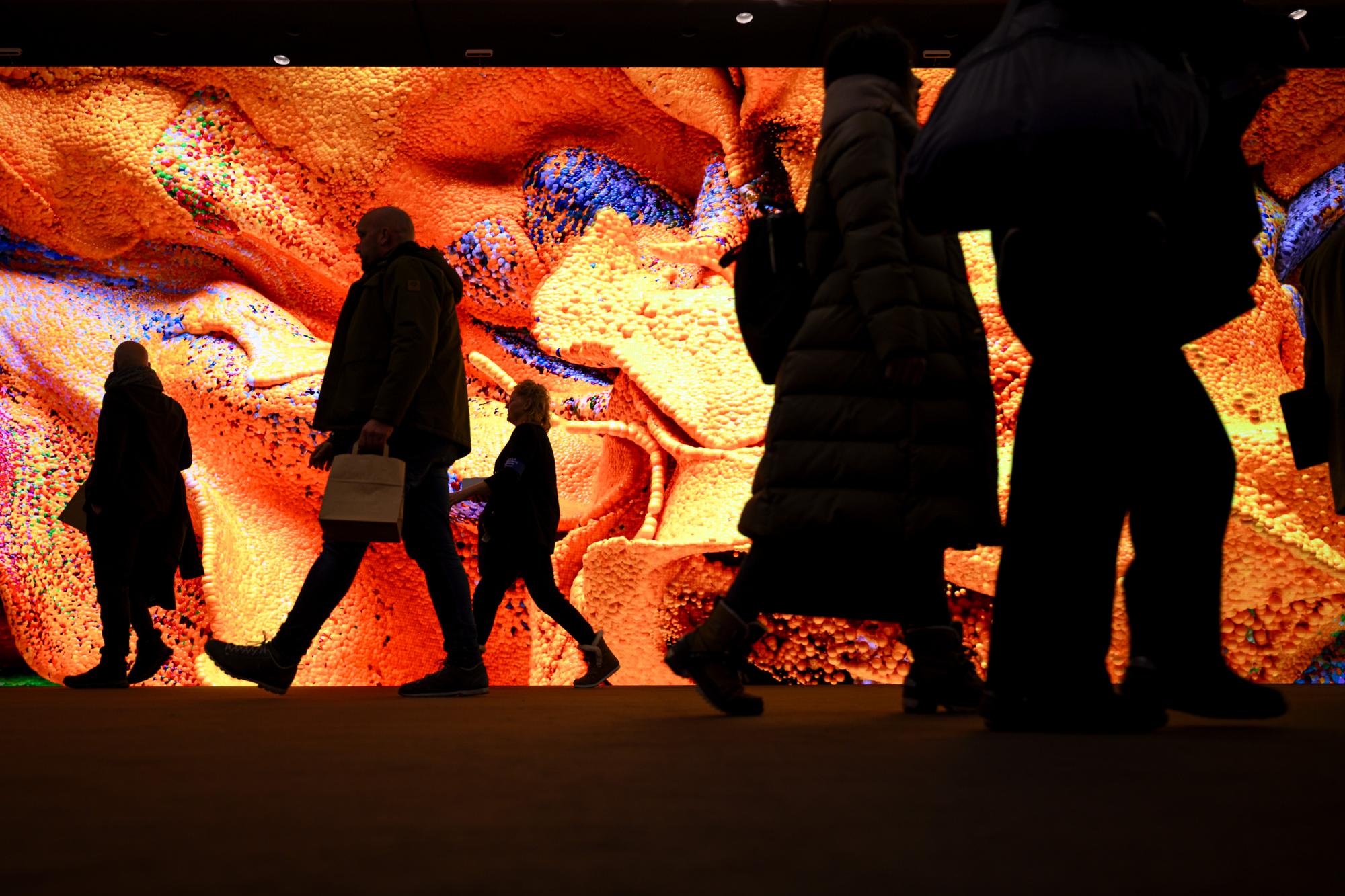 People walk in front of a screen with a artificial intelligence generated artwork by Turkish American media artist Refik Anadol inside the Congress Center on the eve the 54th annual meeting of the World Economic Forum, WEF, in Davos, Switzerland, Sunday, January 14, 2024. The meeting brings together entrepreneurs, scientists, corporate and political leaders in Davos under the topic "Rebuilding Trust" from 15 to 19 January. (KEYSTONE/Laurent Gillieron)