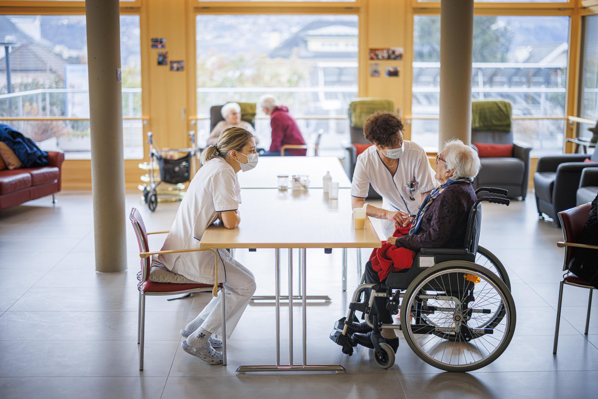 Deux infirmieres parlent avec une residente ce lundi 22 janvier 2024 a l'EMS Saint-Francois a Sion. Une convention collective de travail (CCT) pour le domaine des soins de longue duree (EMS et CMS) a ete signee ce lundi dans le cadre de la mise en ?uvre de l?initiative populaire federale pour des infirmiers forts. (KEYSTONE/Valentin Flauraud)