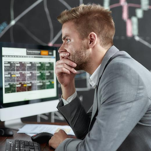 Portrait of successful trader looking focused while sitting in front of monitors in the office. Blackboard full of charts and data analyses in background. Stock trading, business concept. Side view