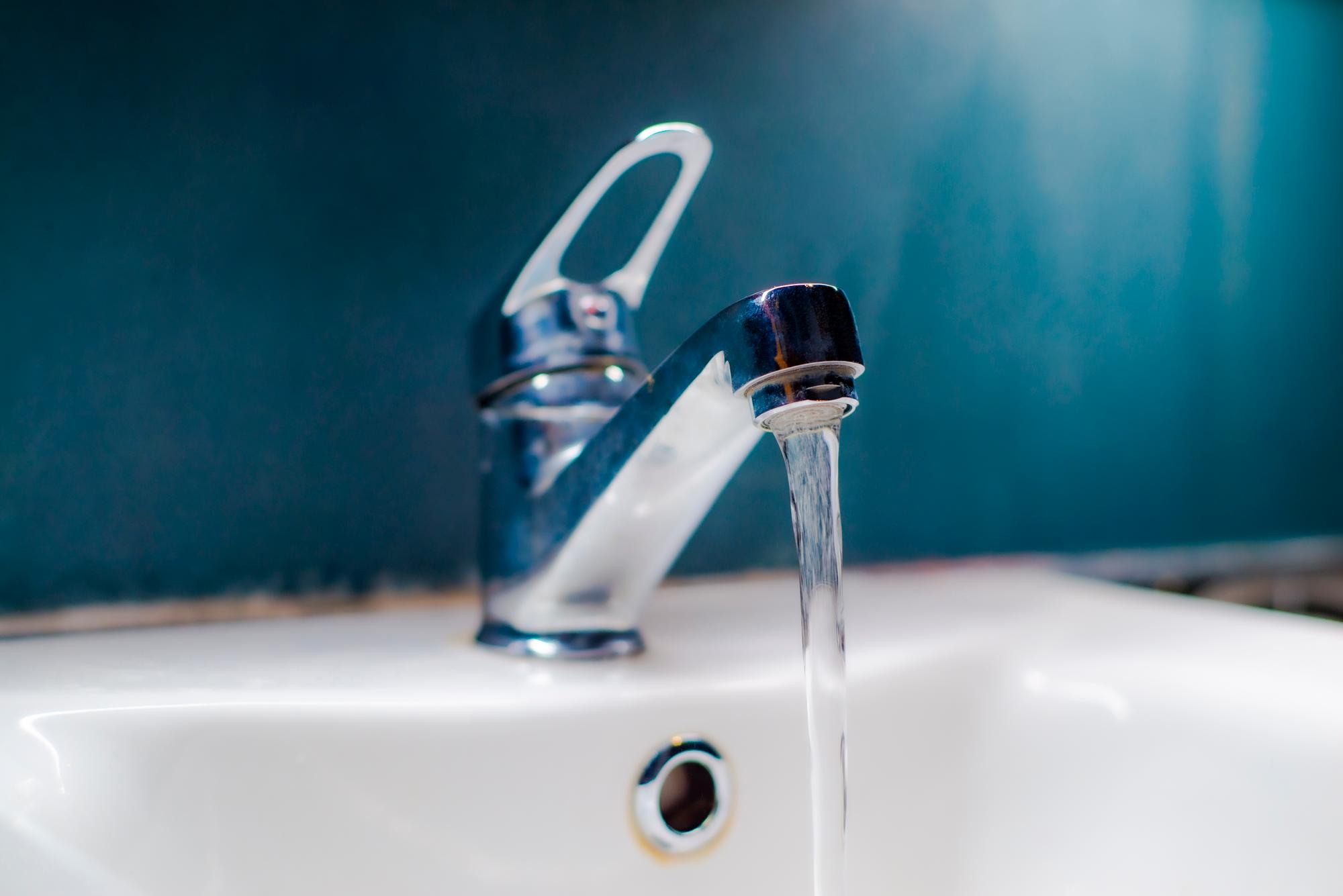 Water running from a faucet. Faucet with flowing water, blue tone.