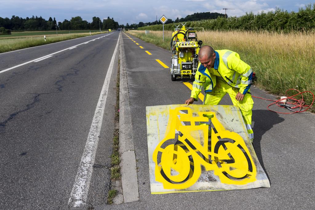 Des ouvriers tracent un pictogramme velo sur une piste cyclable entre Rolle et Gland le vendredi 12 juin 2020 a Rolle. Le canton de Vaud a decide d'accelerer la mise en oeuvre du reseau cyclable cantonal. Pendant l'ete, il creera des bandes cyclables et pistes cyclables provisoires sur plus de 100 kilometres hors des localites. (KEYSTONE/Jean-Christophe Bott)