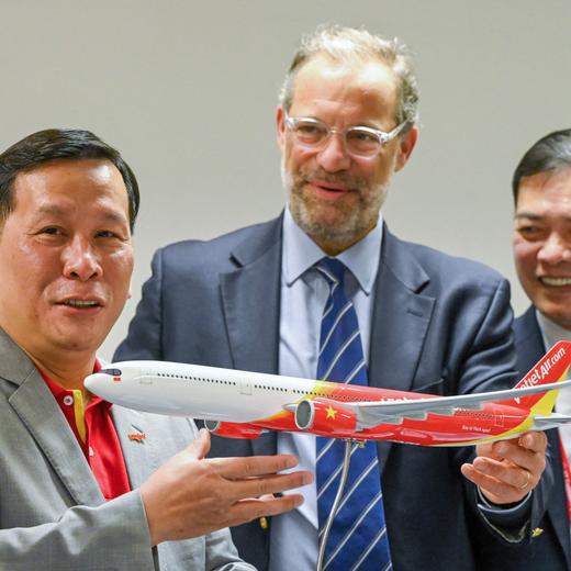 Benoit de Saint-Exupery (C), Airbus executive vice president of sales of commercial aircraft, presents a model airliner as a gift to Vietjet CEO Dinh Viet Phang (L) after a signing ceremony at the Singapore Airshow in Singapore on February 22, 2024. European aviation giant Airbus said February 22 that Vietnamese airline Vietjet Air has agreed to buy 20 of its A330-900 planes. (Photo by Roslan RAHMAN / AFP)