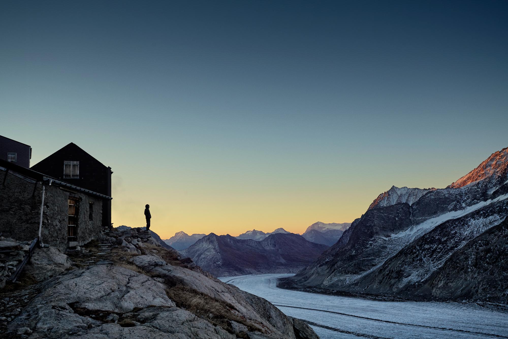 Hiker silhouette watching sunrise over mountain range and glacier, Aletsch Glacier, Switzerland